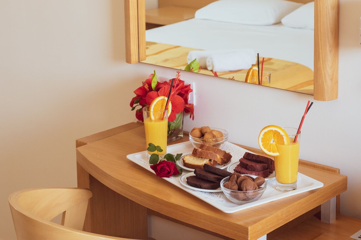 A hotel room with a wooden bed, a bedside table with a tray of breakfast, a mirror, and a wall-mounted light fixture.