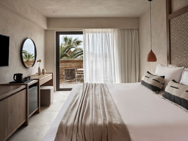 A modern hotel room with a large bed, a desk, a chair, a television, and a view of palm trees through the window. - Stella Blue Seaside Resort (Hersonissos)