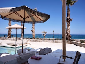 A poolside area with lounge chairs, a table with a book and glass, and a view of the sea. - Stella Blue Seaside Resort (Hersonissos)