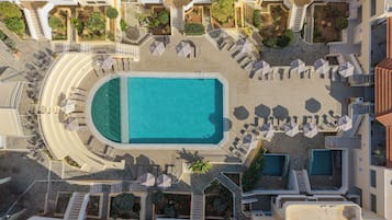 An aerial view of a resort with a central swimming pool, sun loungers, and a landscaped garden area.