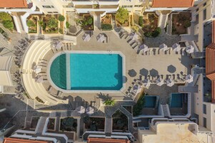 Vista aérea de un resort con piscina central, tumbonas y un jardín ajardinado.