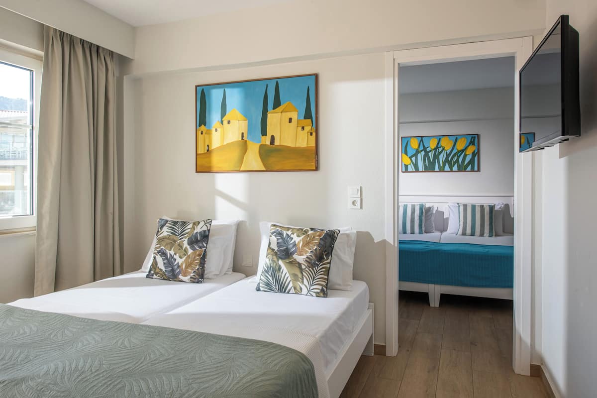 A hotel room with a large bed, two pillows, a painting, a TV, and a view of the city.