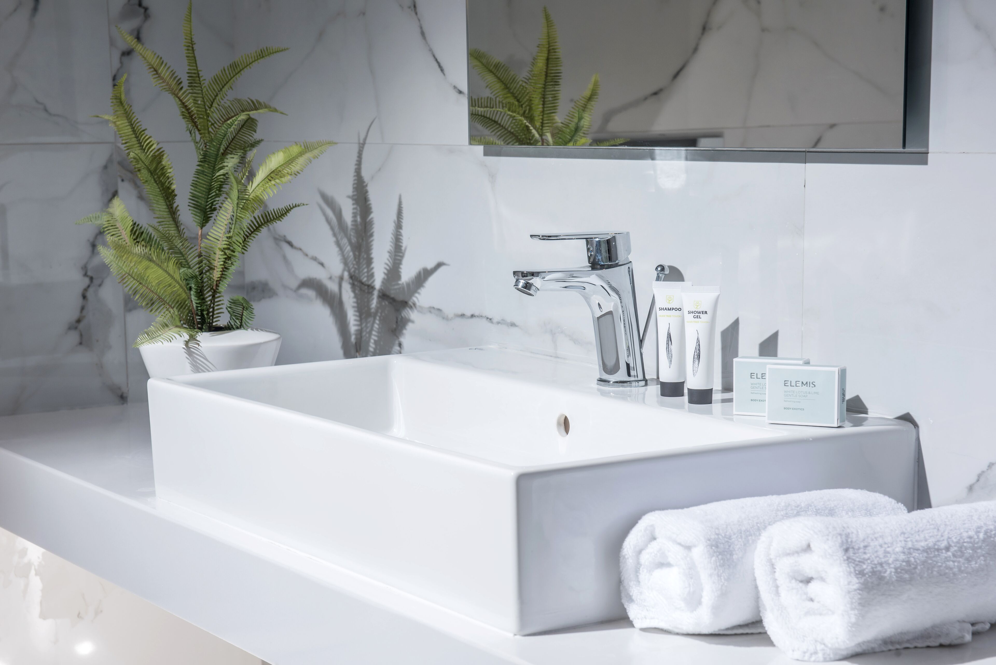 Un baño moderno con un lavabo blanco, grifo cromado y artículos de aseo.