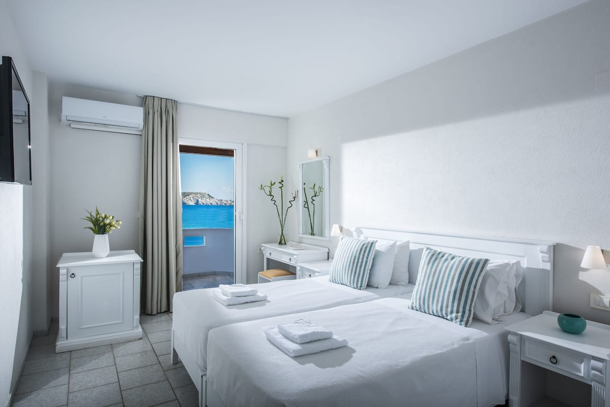 A hotel room with two beds, a desk, a vanity, and a view of the sea.
