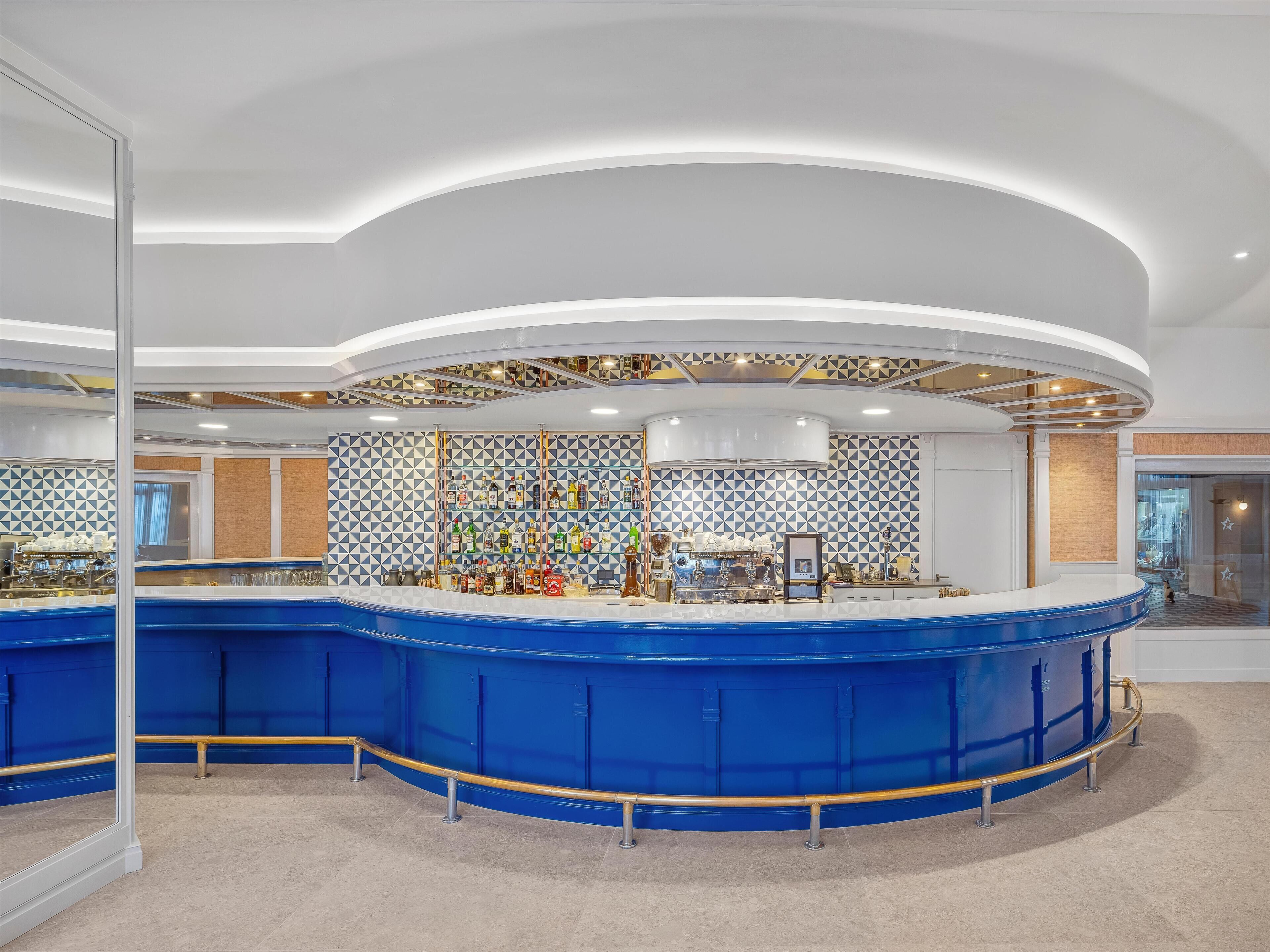 A modern bar area with a curved blue counter, a variety of liquor bottles, and a decorative ceiling.