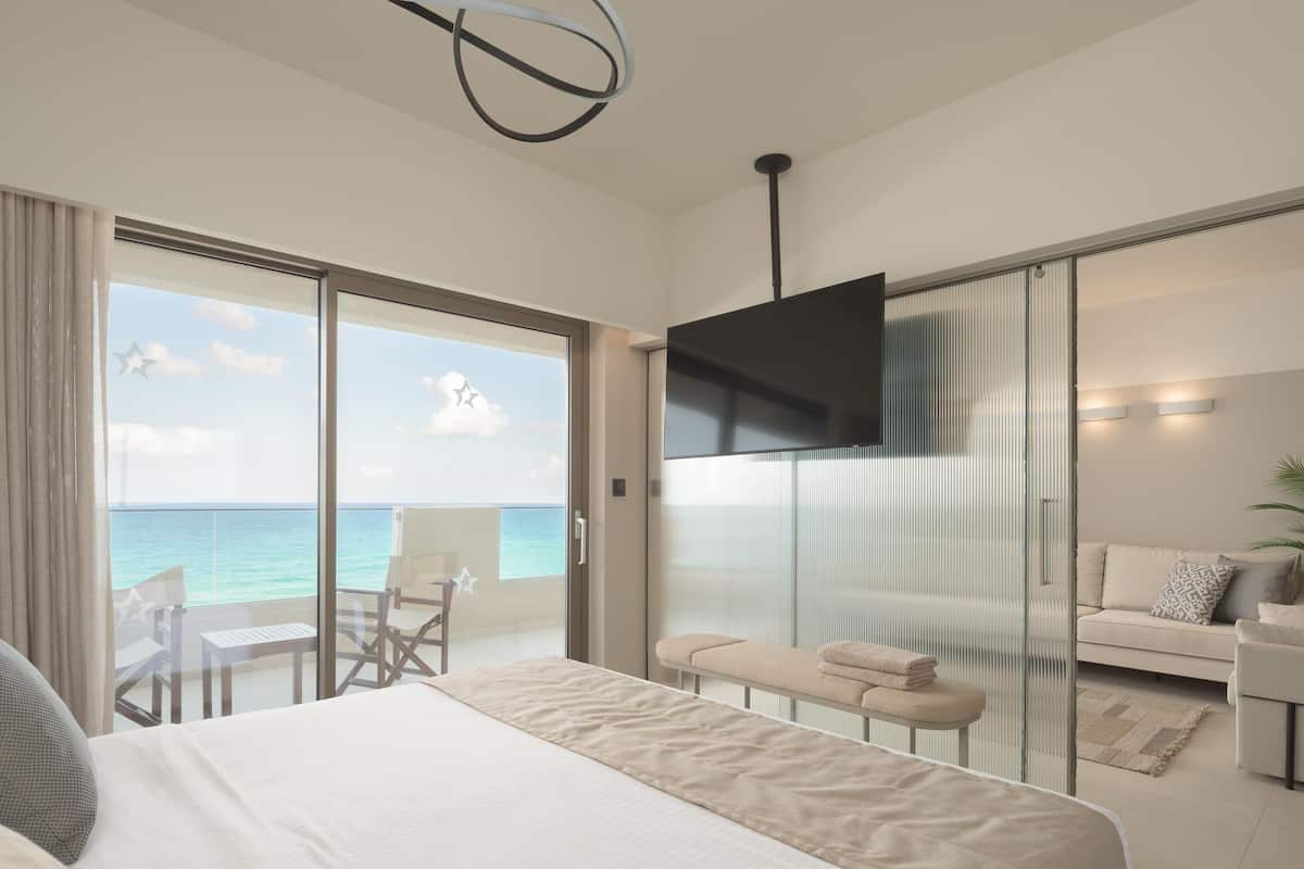 A modern hotel room with a balcony, a bed, a sofa, and a TV.