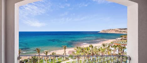 A balcony with a view of a beach and a resort area with rows of sun loungers and umbrellas.