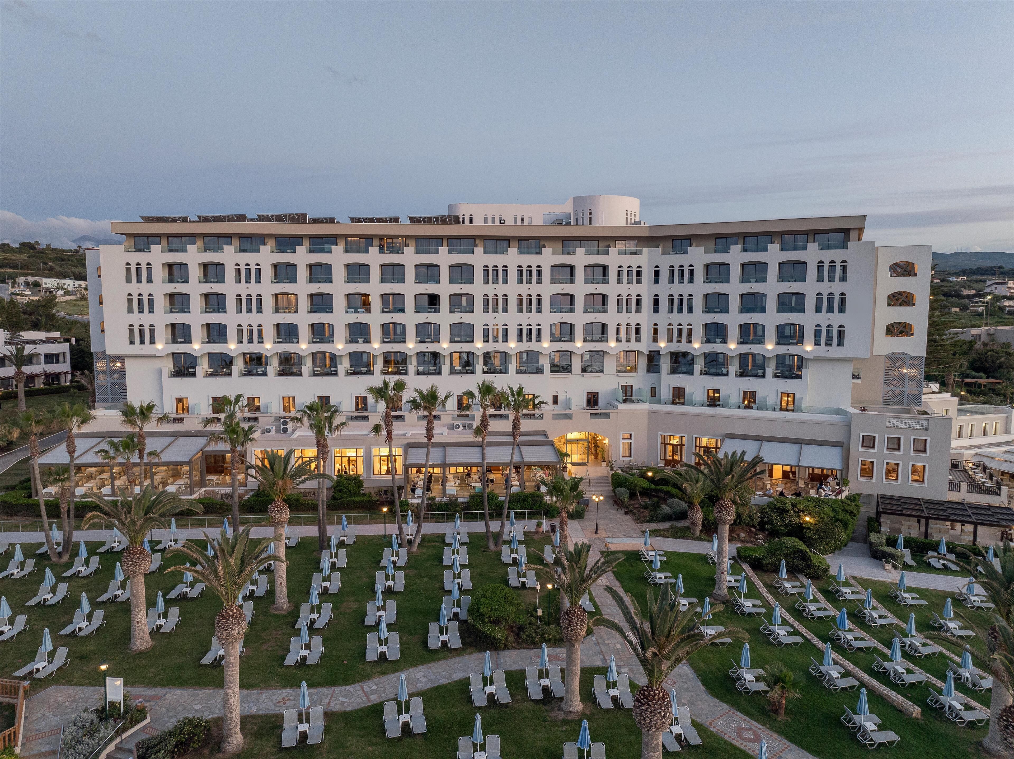 A large hotel with multiple floors, outdoor seating areas with umbrellas, and palm trees.