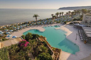 A resort pool area with multiple sun loungers and umbrellas, surrounded by palm trees and a view of the sea. - Creta Star Hotel (Rethymno)