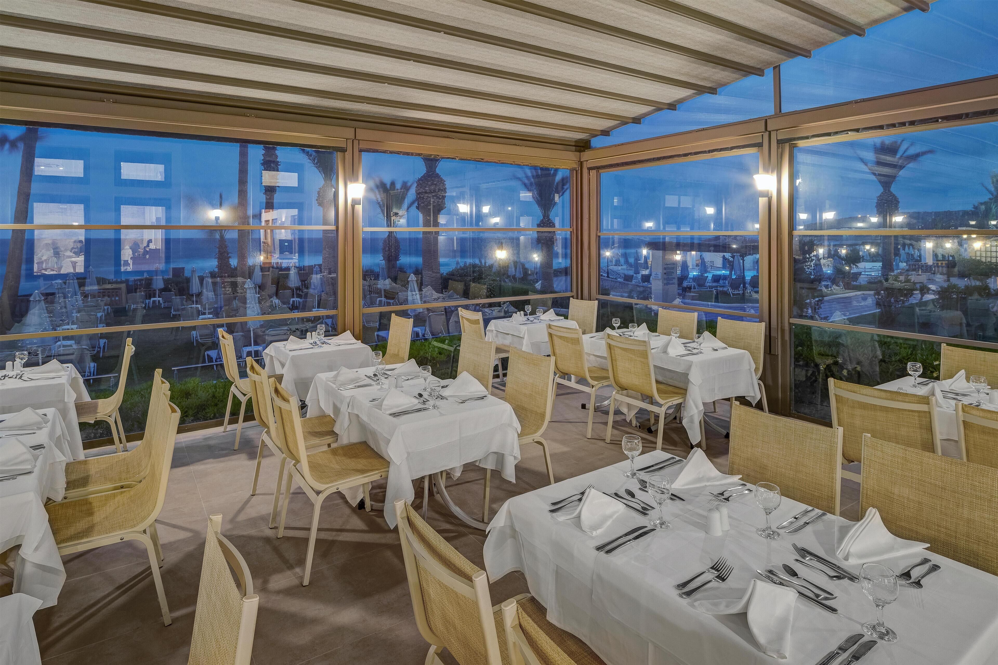 An outdoor dining area with tables set for two, large windows, and a view of the cityscape.