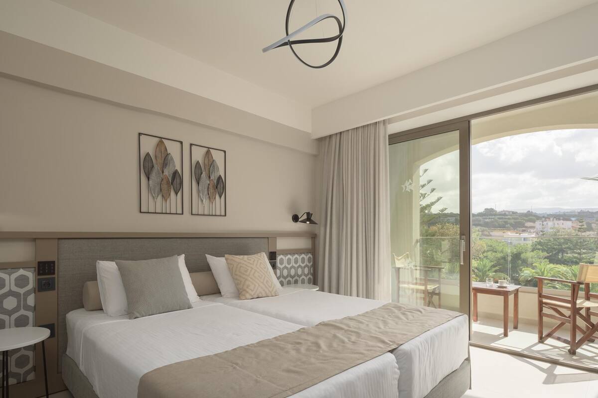 A modern hotel room with two beds, a balcony with a view, and a dining area.