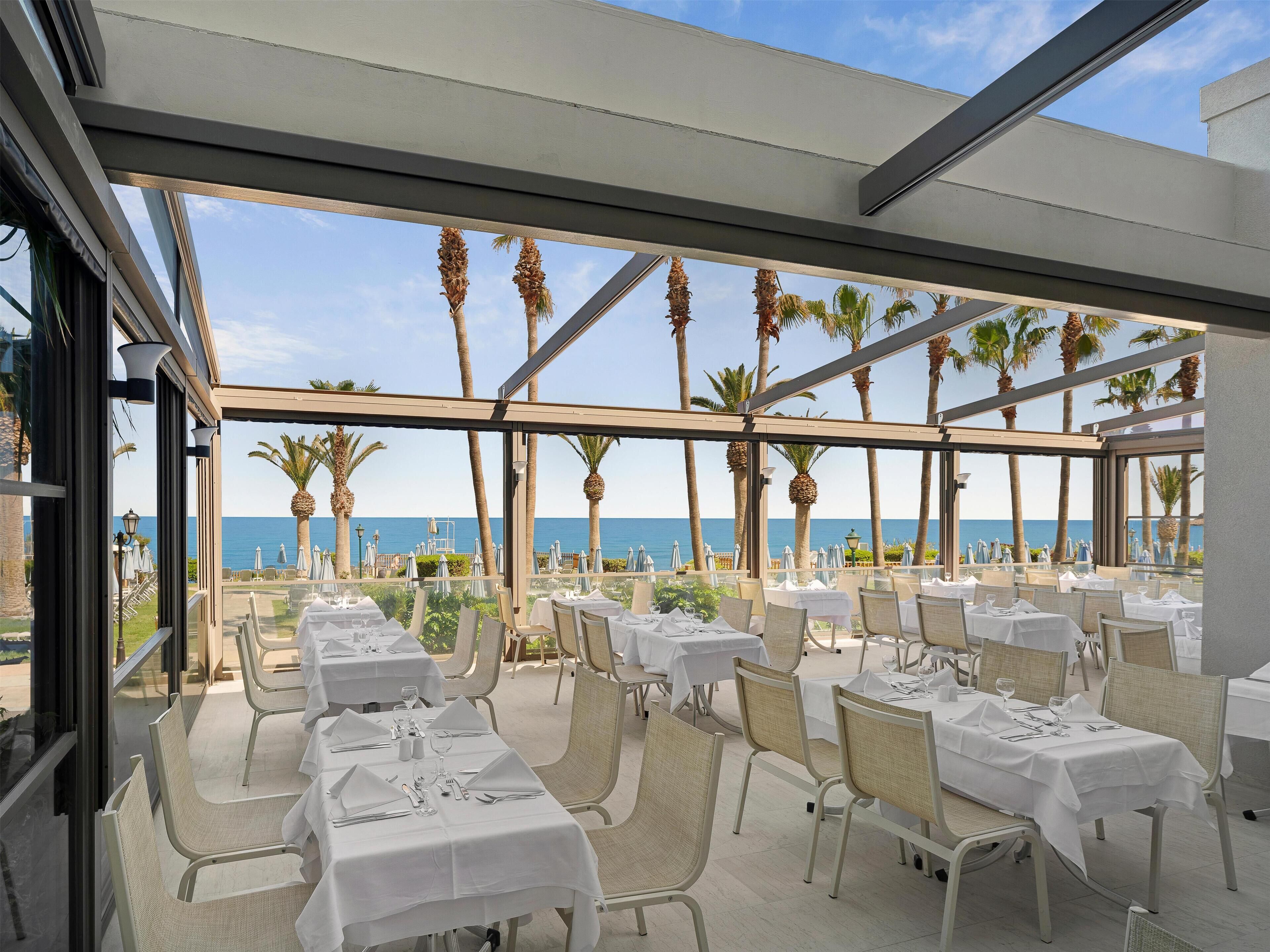 Een restaurant met terras aan zee, met witte tafellaken en rieten stoelen.