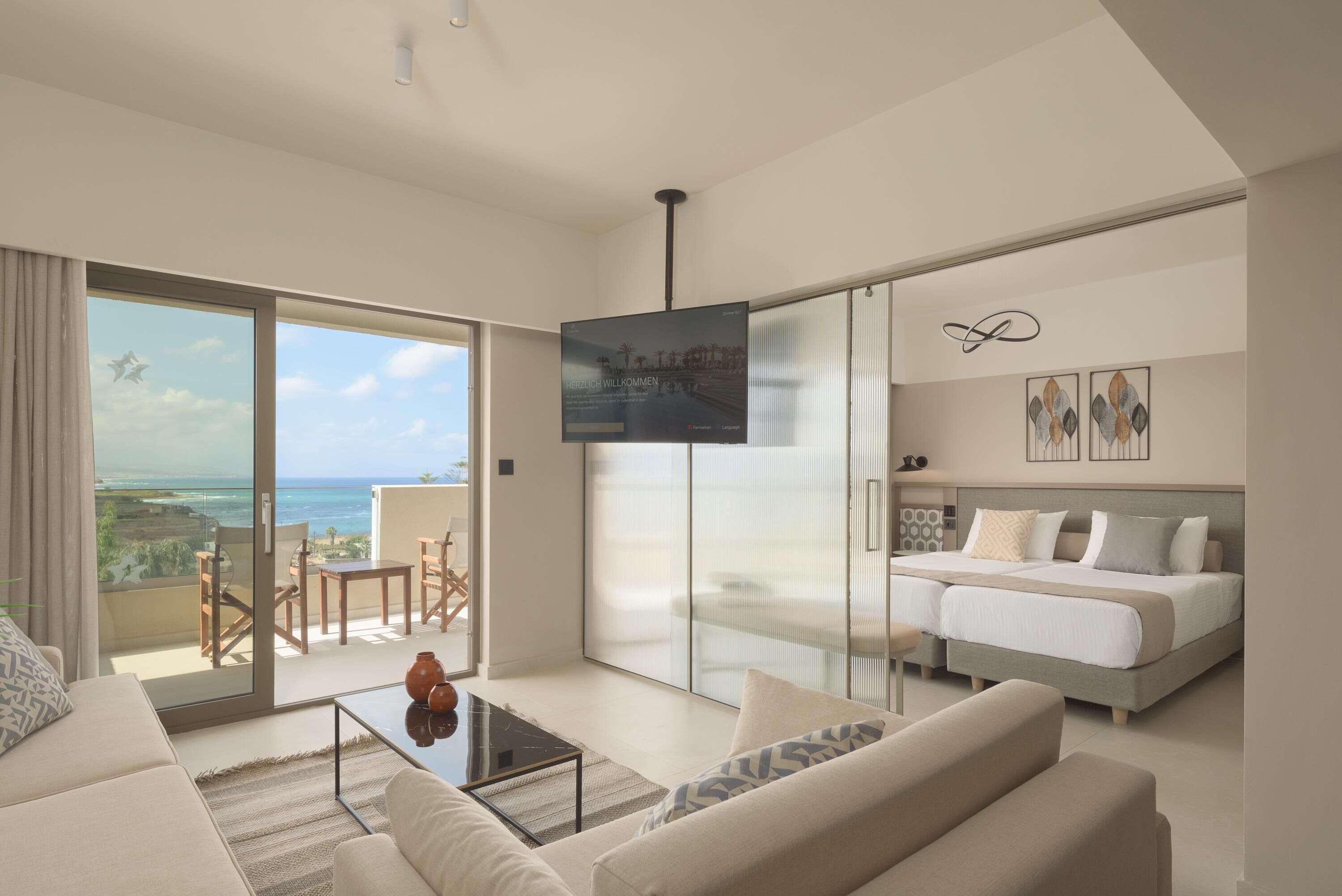 Ein modernes Hotelzimmer mit Balkon, einem Bett, einer Couch und einem Fernseher.