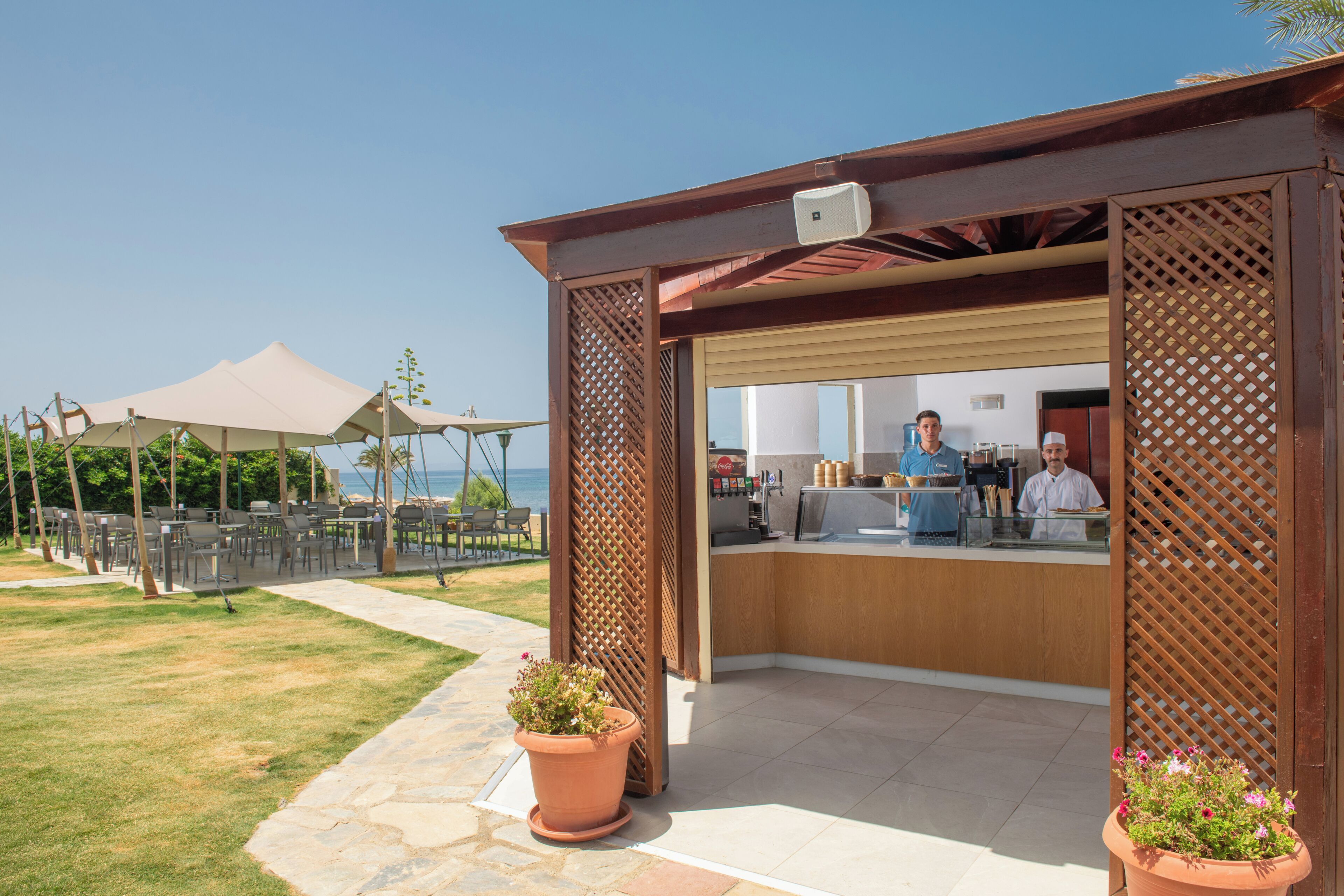 An outdoor cafe with a view of the sea, a bar area, and a seating area with tables and chairs.