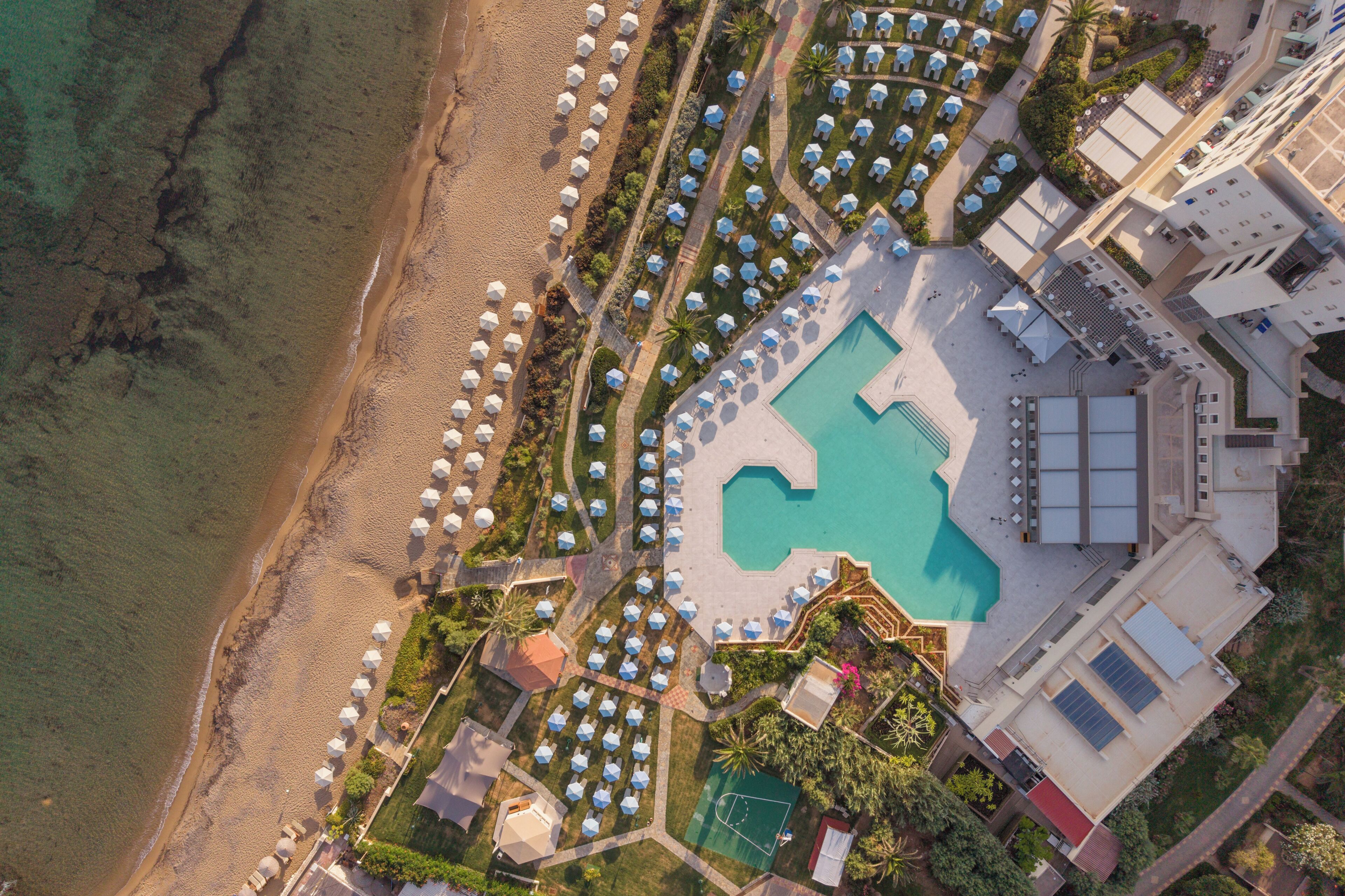 An aerial view of a resort with a swimming pool, beach umbrellas, and a beachfront.