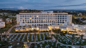 A large hotel with multiple floors, a well-lit courtyard with rows of lounge chairs and umbrellas, and a view of the surrounding landscape. - Creta Star Hotel (Rethymno)