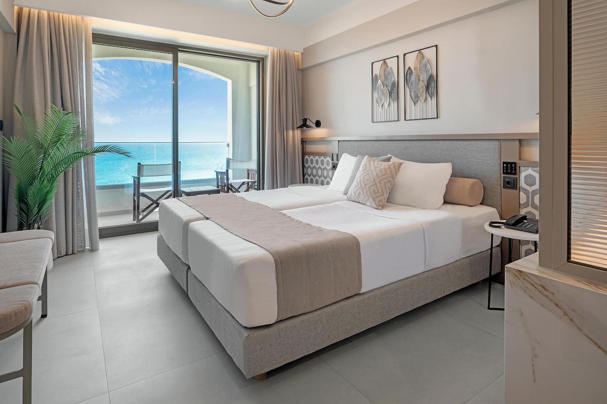 A modern hotel room with a large bed, a bedside table, a lamp, and a view of the ocean.