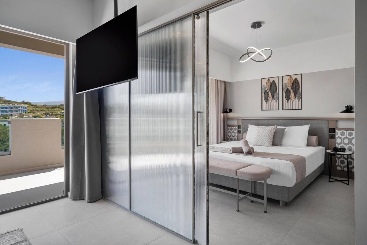 A modern bedroom with a bed, a TV, and a balcony with a view.