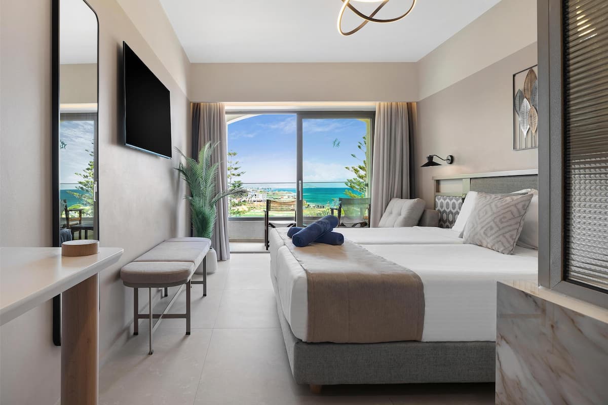 A modern hotel room with a bed, a desk, and a large window offering a view of the ocean.