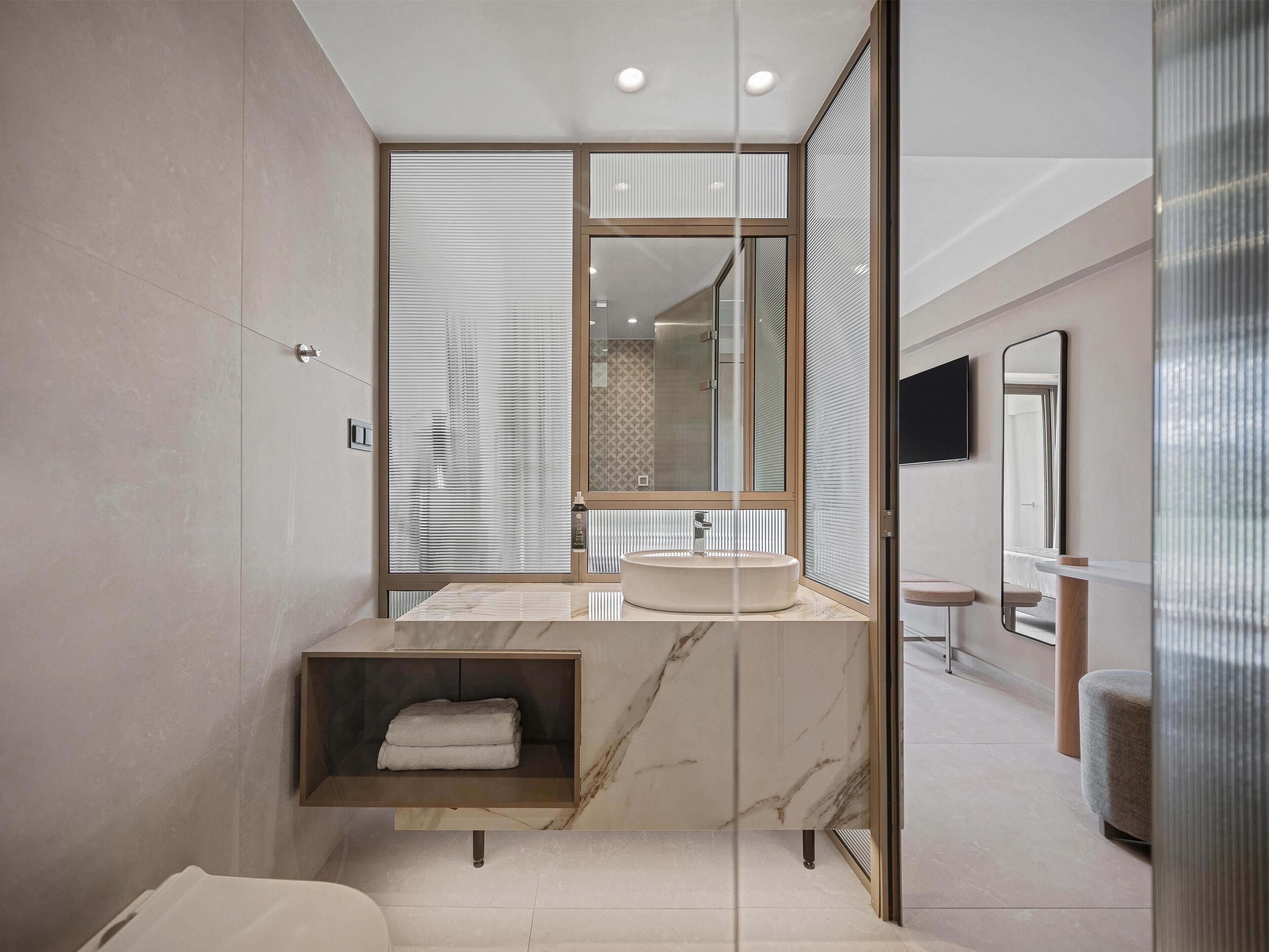 A modern bathroom with a marble vanity, a built-in shelf, and a large mirror.