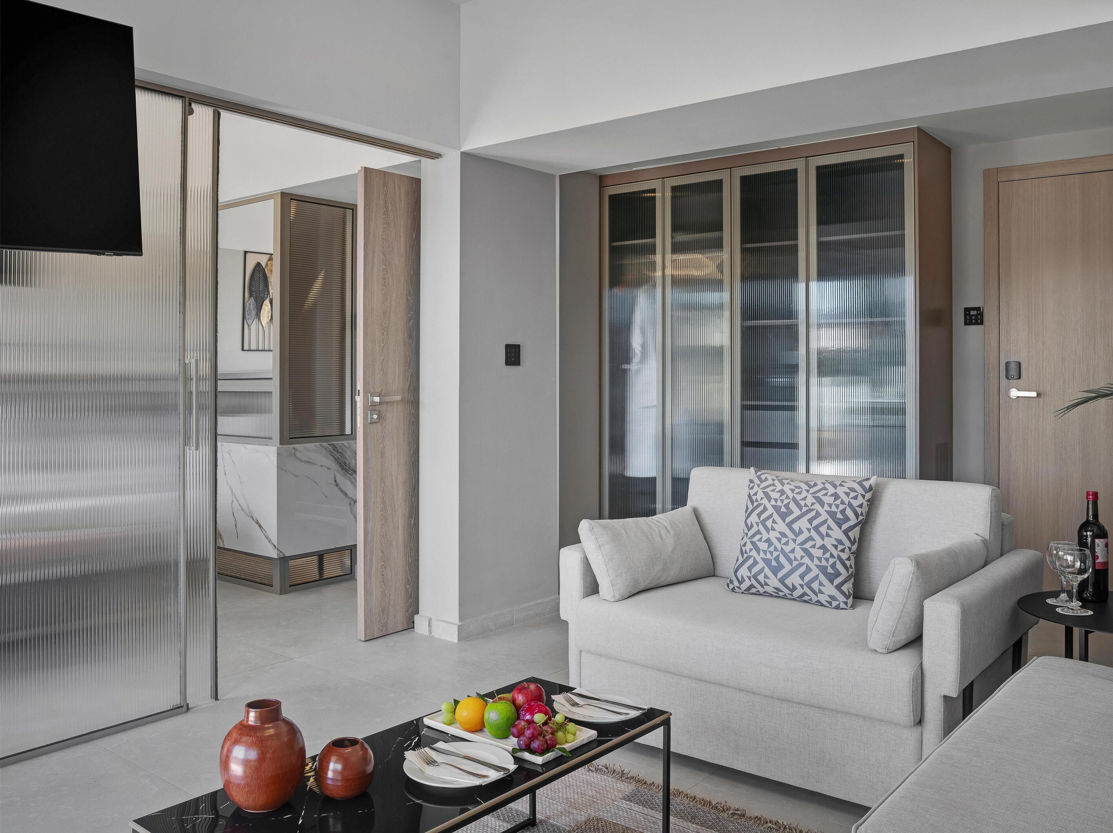 A modern living room with a sofa, a coffee table with fruit and cutlery, and a TV.