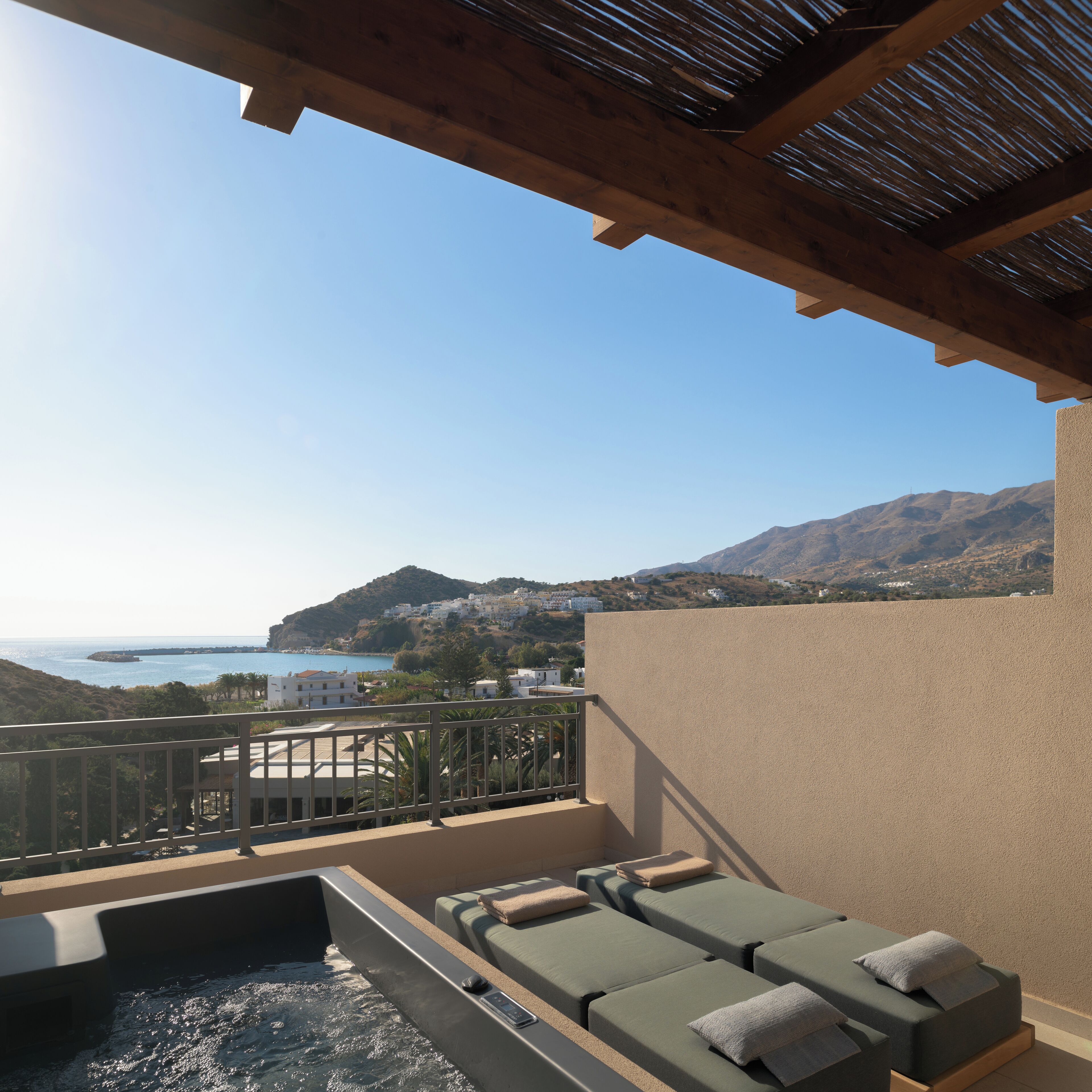 A balcony with a hot tub, lounge chairs, and a view of the sea and hills.