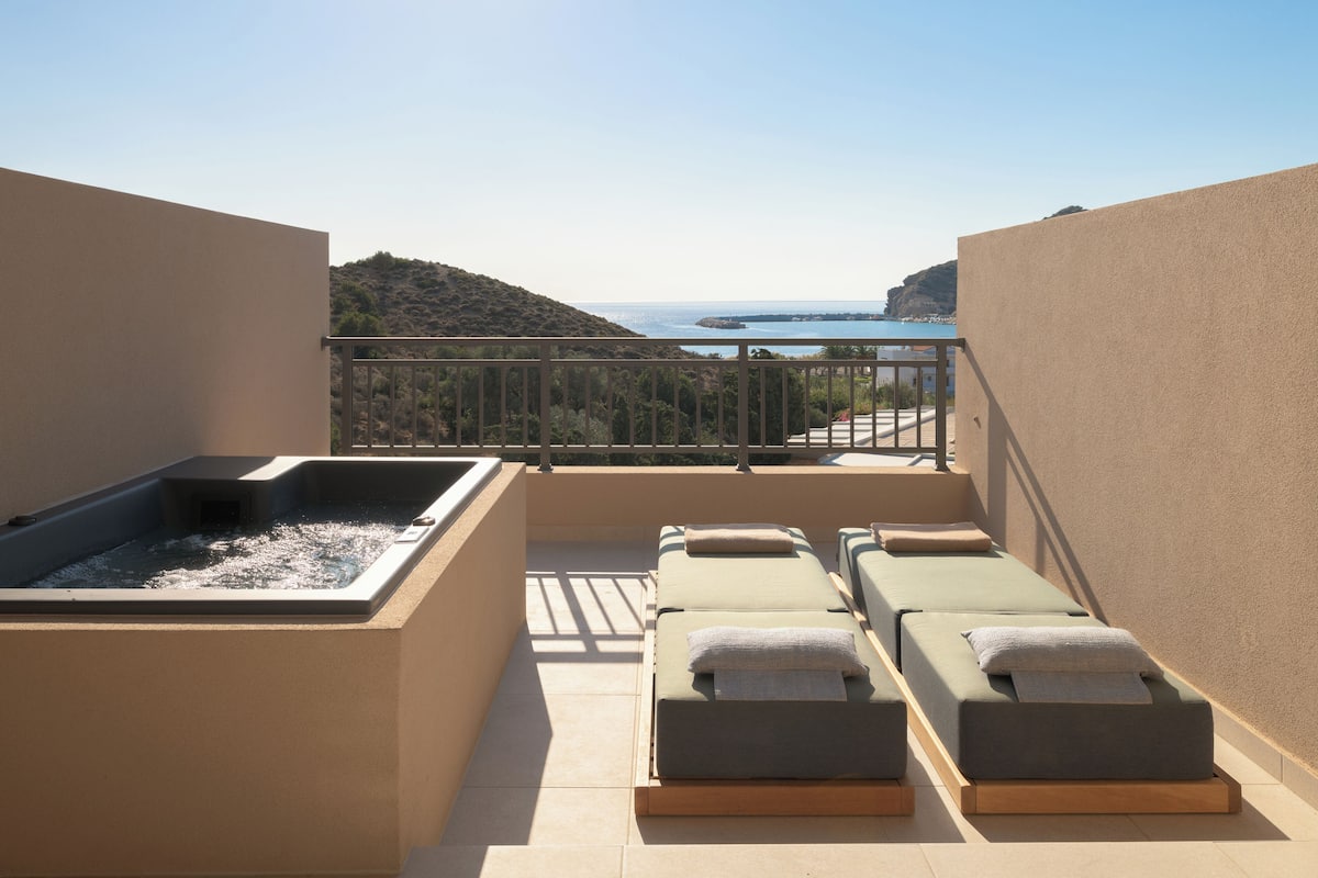 A sunlit balcony with a hot tub, lounge chairs, and a view of the sea.