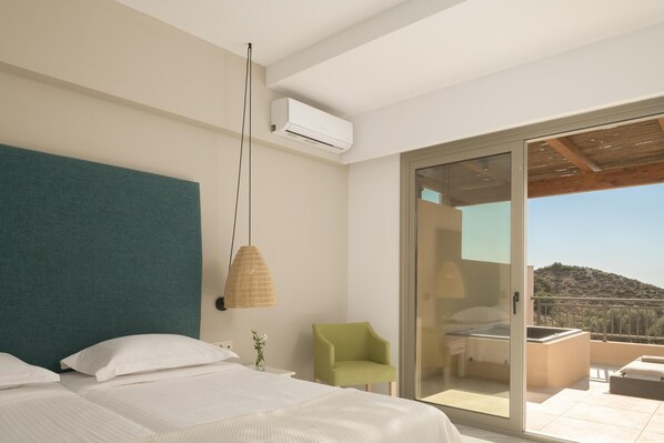 A modern hotel room with a large bed, a green armchair, and a balcony with a view of the hills.
