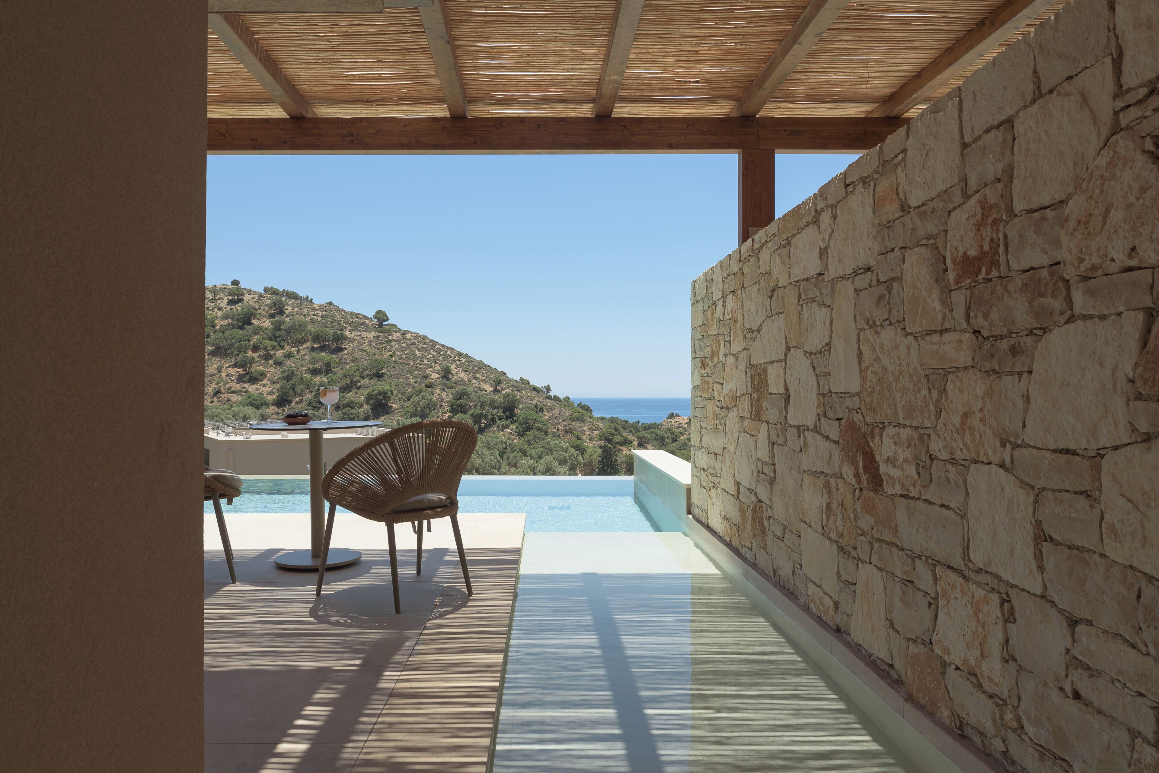 A stone wall, a wooden ceiling, and a view of a hill and sea.