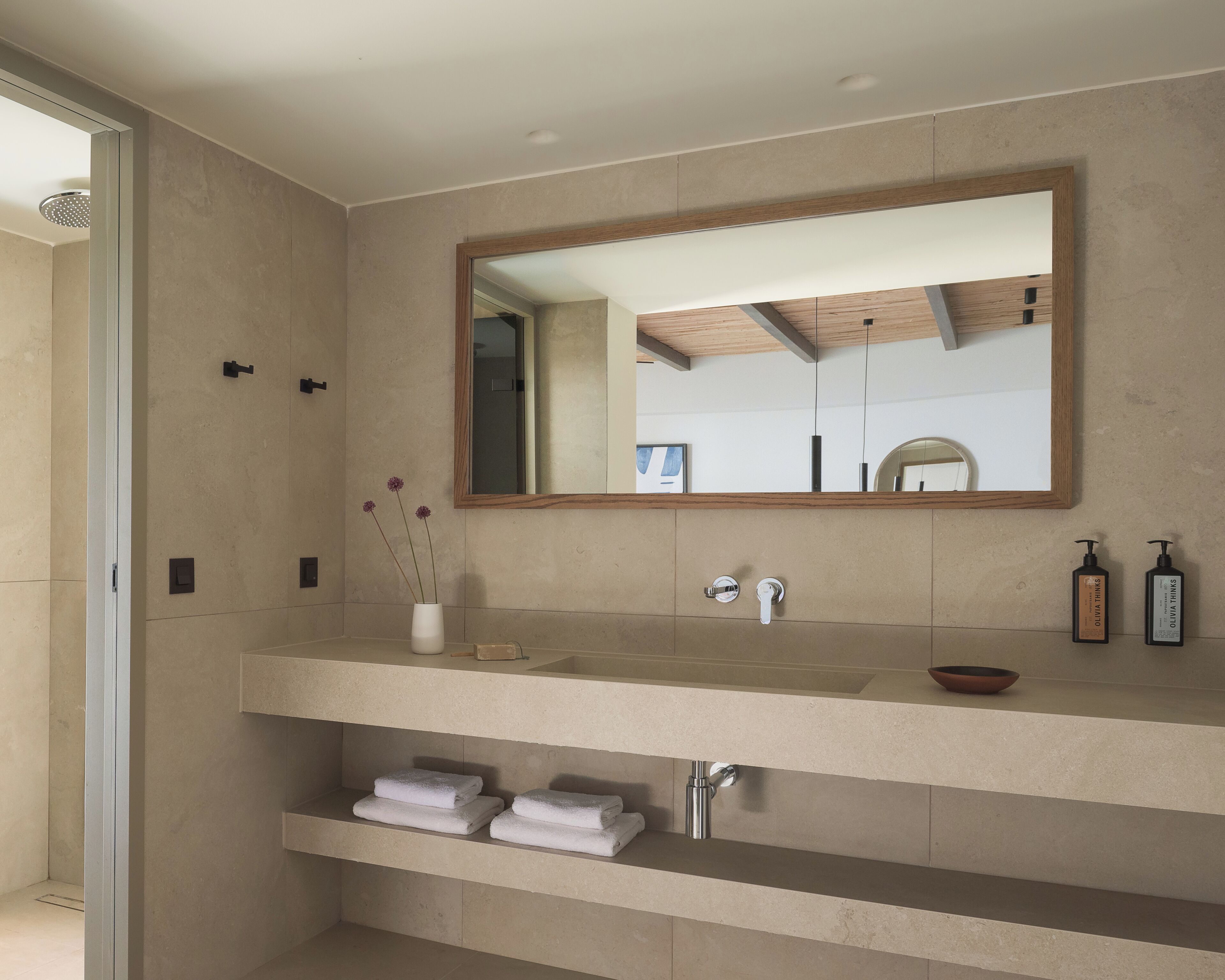 A modern bathroom with a large mirror, a sink with a bowl, and two shelves with folded towels.