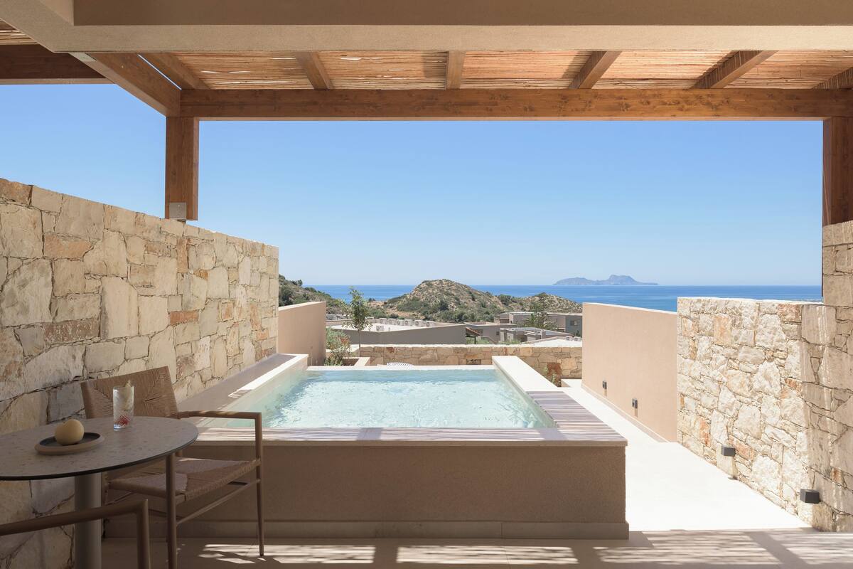 A stone-walled outdoor area with a hot tub and a table with chairs.