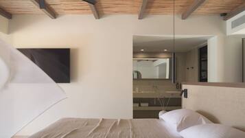 A bedroom with a wooden ceiling, a bed with white bedding, a large mirror, and a bathroom visible through an open door.