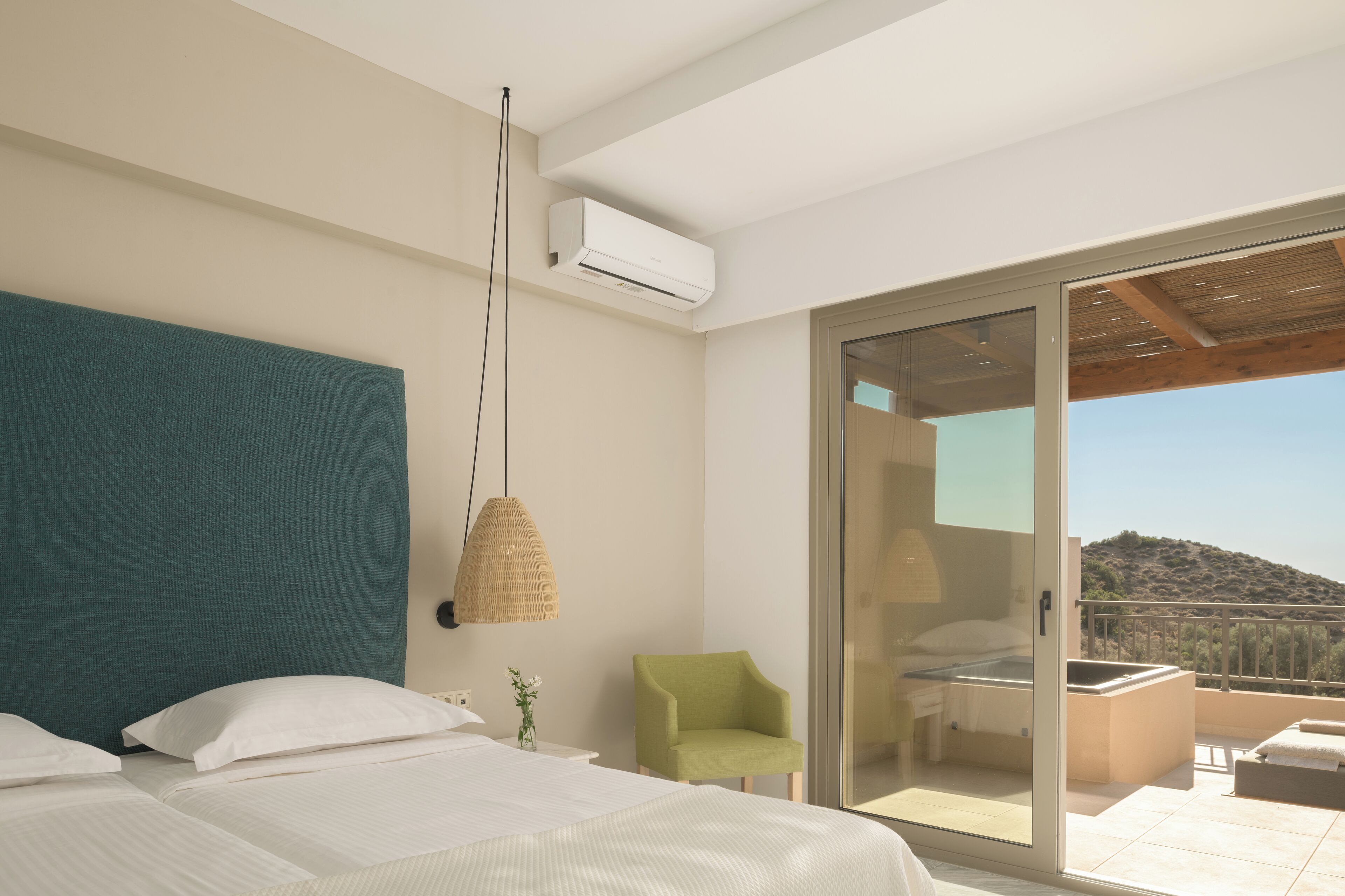 Un dormitorio moderno con una cama grande, una silla verde y un balcón con vistas a las colinas.