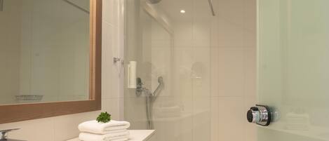 A modern bathroom with a glass shower enclosure, a large mirror, and a sink with stacked towels.