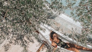 A hammock under olive trees, a person lying in it, and a stone pathway. - Paralos Irini Mare (Agios Vasileios)