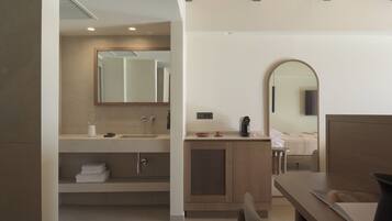 A modern bathroom with a large mirror, a sink, and a toilet. There is a wooden vanity and a bedside table with a book.