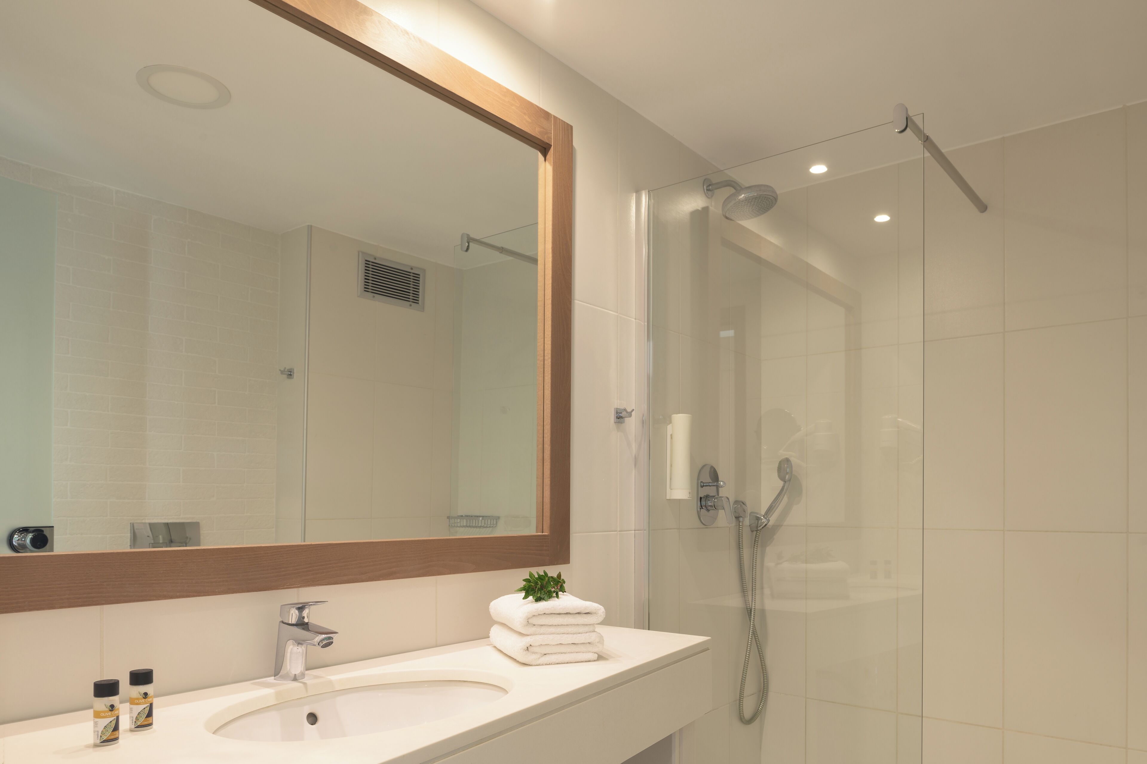 A modern bathroom with a large mirror, a sink, and a glass-enclosed shower.