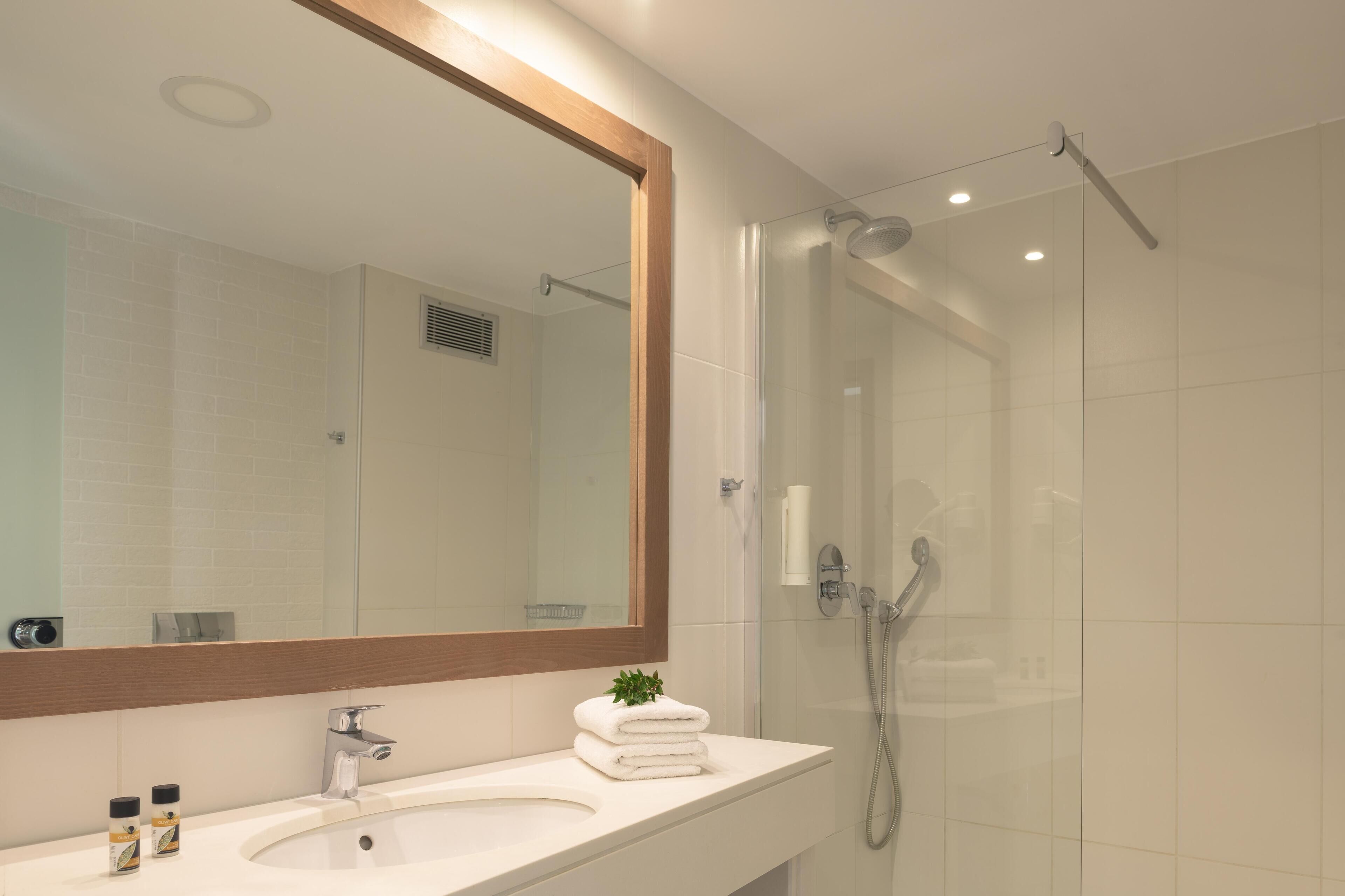 Un baño moderno con un espejo grande, un lavamanos y una ducha con paredes de vidrio.