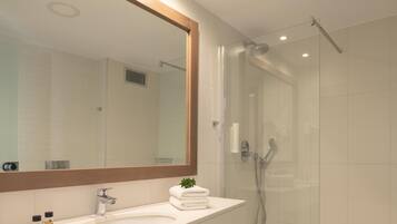 Un baño moderno con un espejo grande, un lavamanos y una ducha con paredes de vidrio.