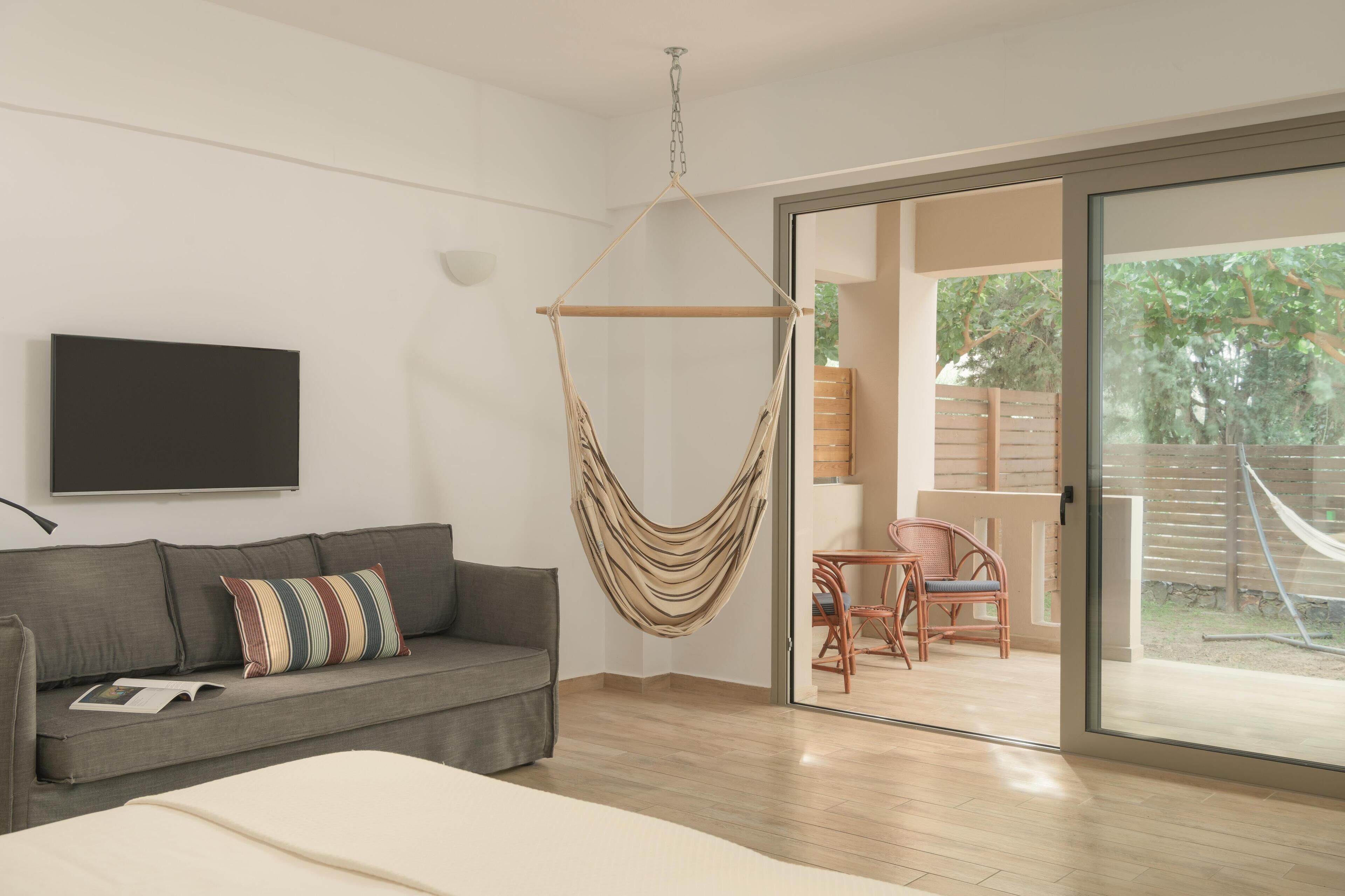 A modern bedroom with a grey sofa, a hanging hammock, and a sliding glass door leading to a balcony.