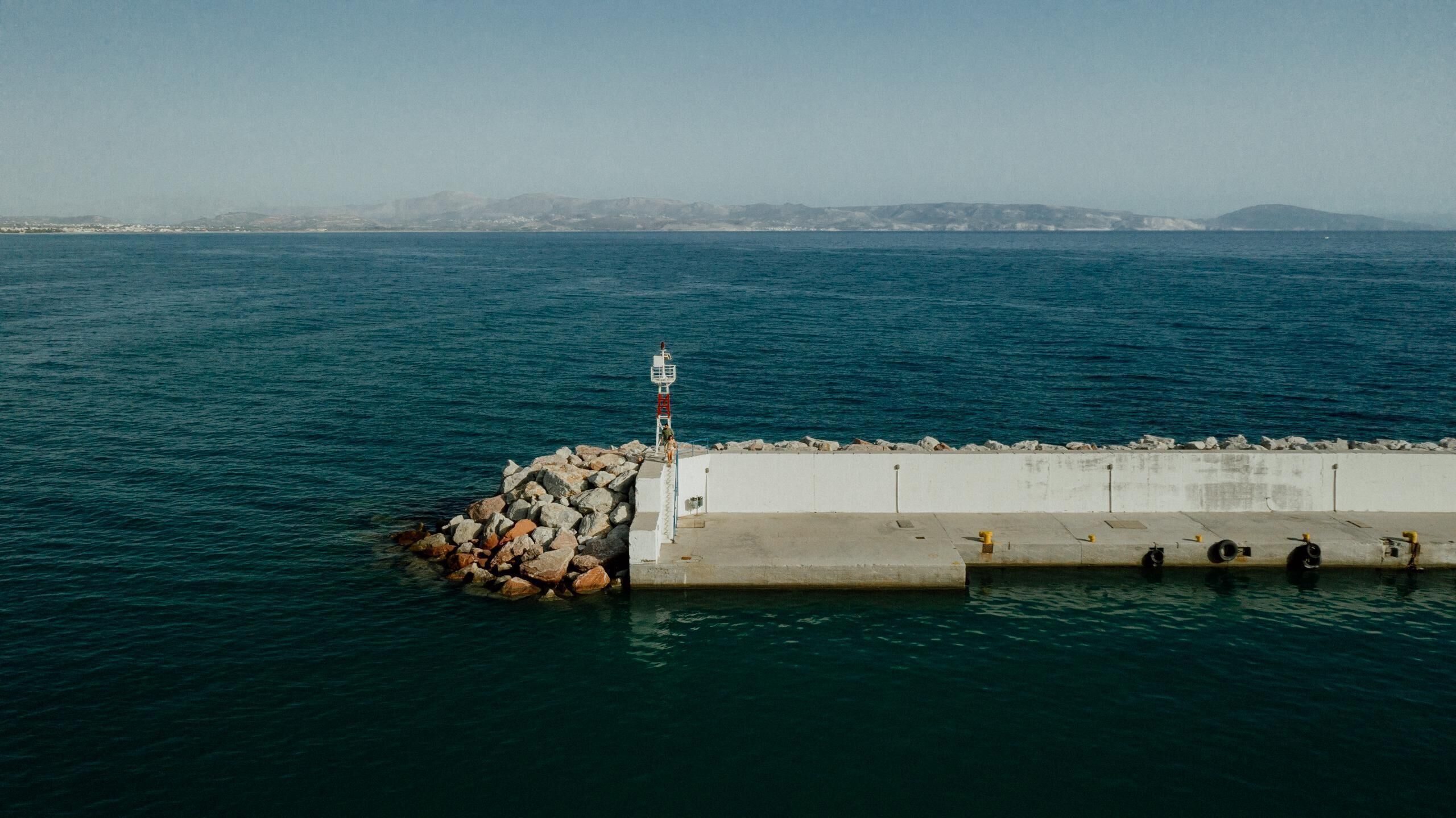 A coastal pier with a lighthouse, rocky breakwater, and calm sea.