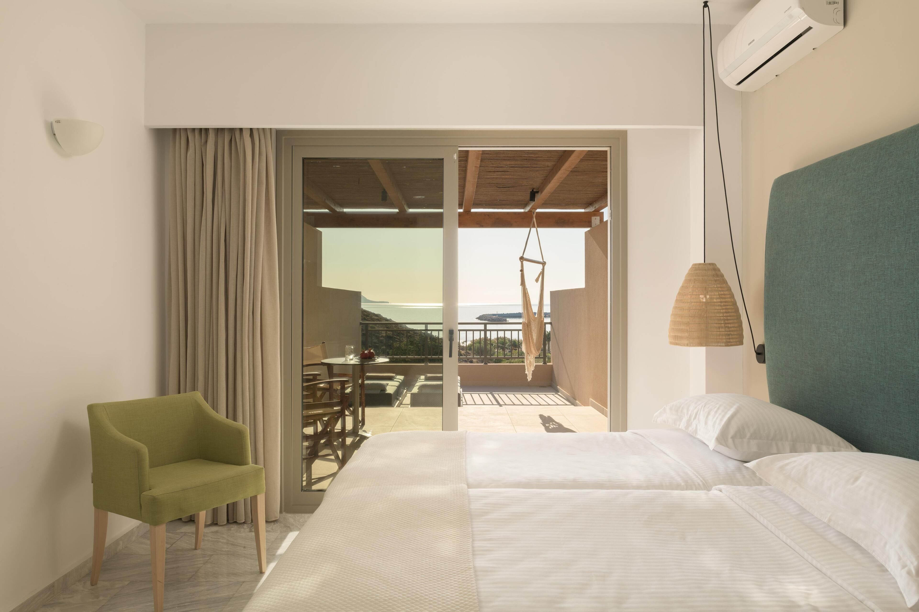 A hotel room with a bed, a chair, a table, and a view of the outdoors.
