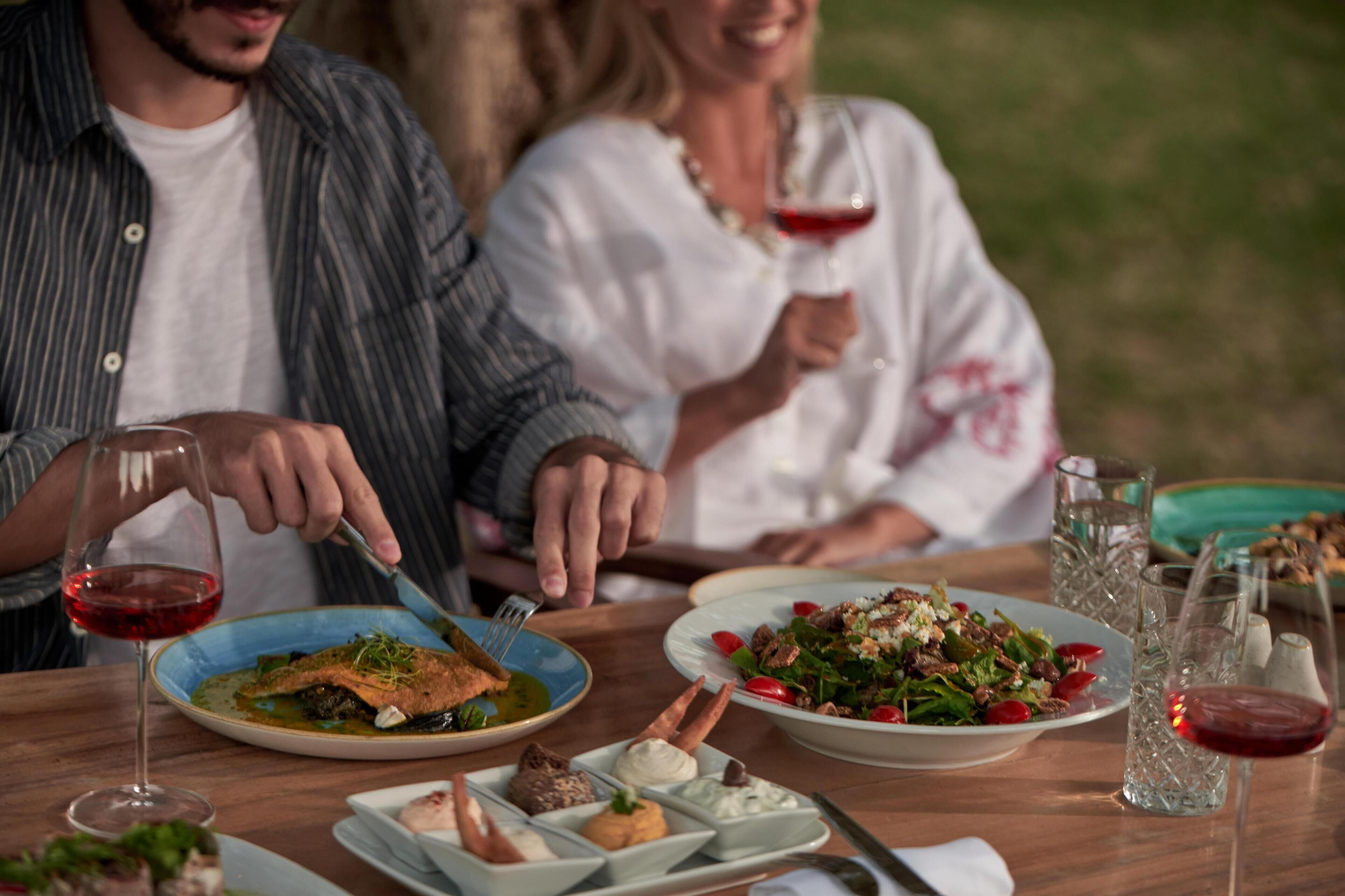 A dining table with plates of food, glasses of red wine, and a fork.