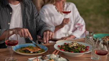 A dining table with plates of food, glasses of red wine, and a fork.