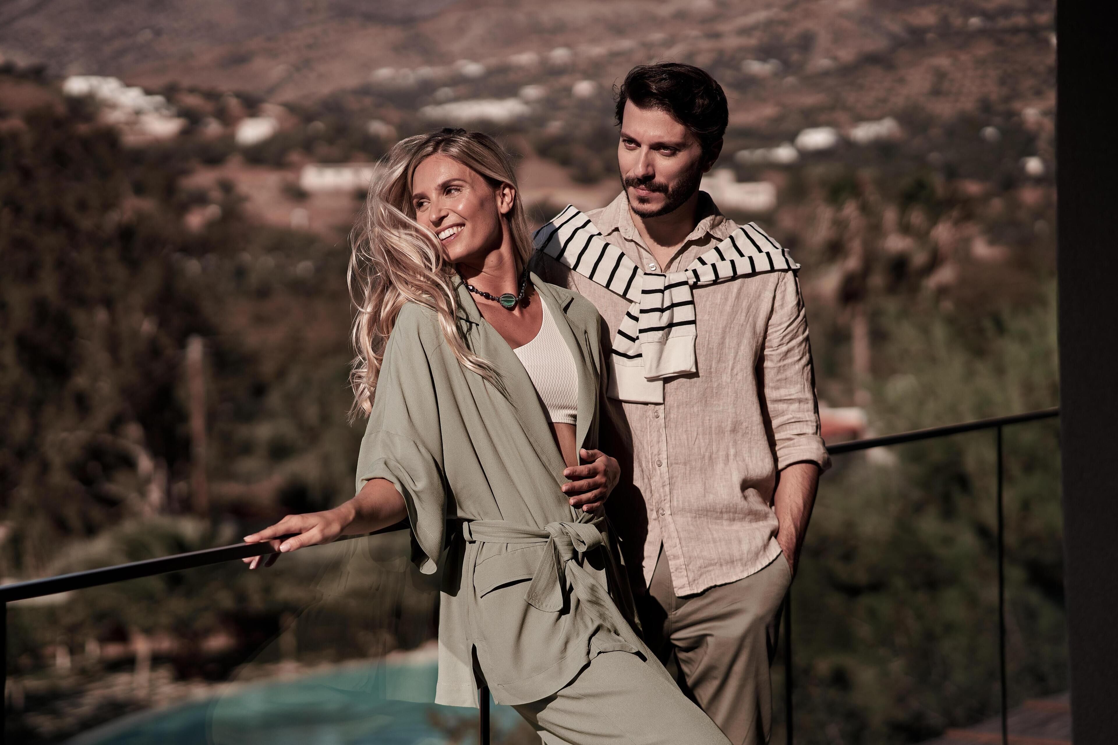 Two people standing on a balcony with a view of a mountainous landscape.