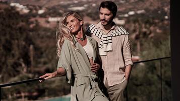 Two people standing on a balcony with a view of a mountainous landscape.
