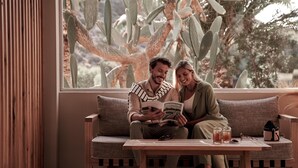 A couple sitting on a wooden bench by a window with a cactus view. - Paralos Irini Mare (Agios Vasileios)