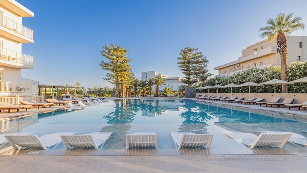 Ein Pool mit Liegestühlen, Palmen und einem Gebäude mit Balkonen.