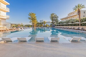 A swimming pool with lounge chairs, palm trees, and a building with balconies. - Marilena Hotel - All inclusive (Malevizi)