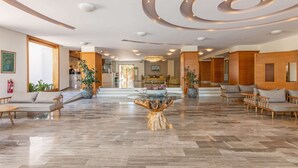 Eine großzügige Lobby mit einem zentralen Holztisch, Sitzbereichen und einem modernen Deckenstil.